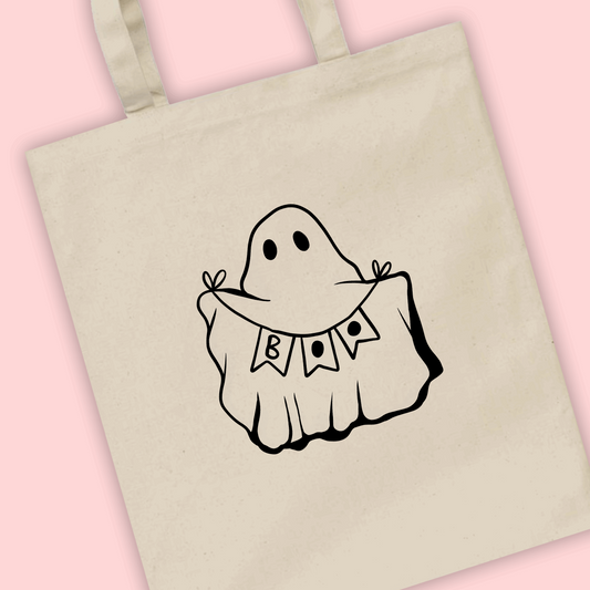 A tote bag featuring an illustration of a cute ghost holding a banner/bunting saying Boo
