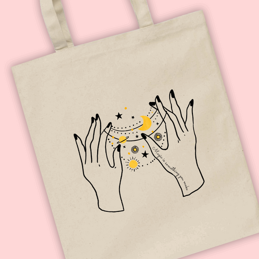 A natural tote bag with an illustration of two celestial hands with stars and moons