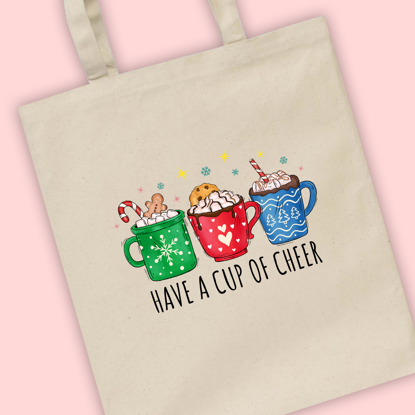 A natural tote bag with Cups Of Cheer written with an illustration of three Christmas hot chocolates