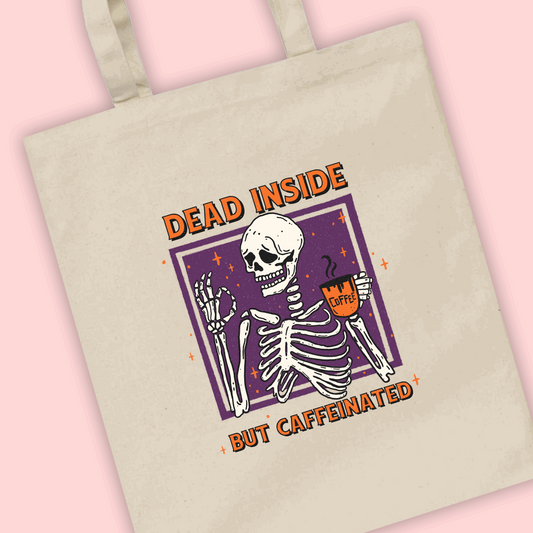 A natural tote bag with an illustration of a skeleton drinking coffee with ‘dead inside but caffeinated’ written