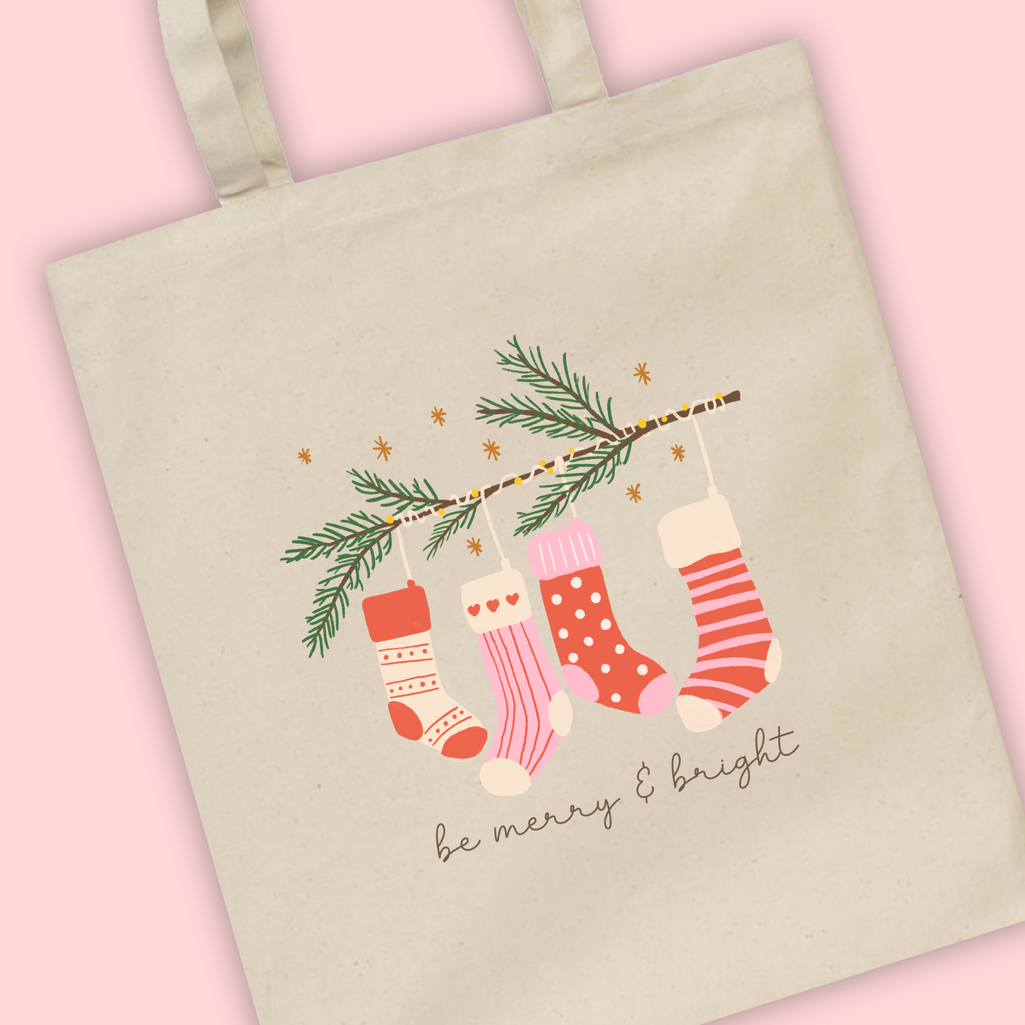 A tote bag with an illustration of stockings with Be Merry and Bright written