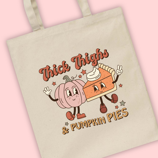 A natural tote bag with Thick Thighs and Pumpkin Pies written and an illustration of a pumpkin pie with smiley faces