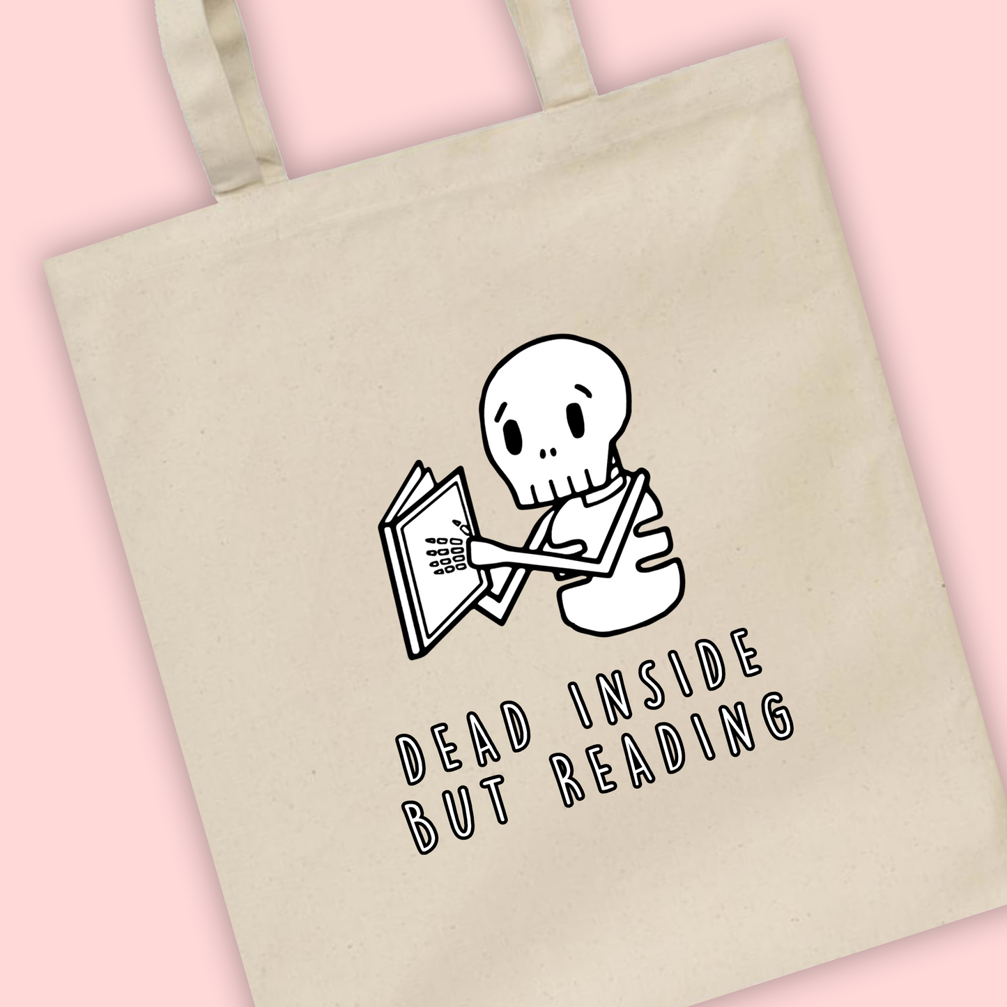 A natural tote bag with an illustration of a skeleton reading a book with ‘dead inside but reading’ written